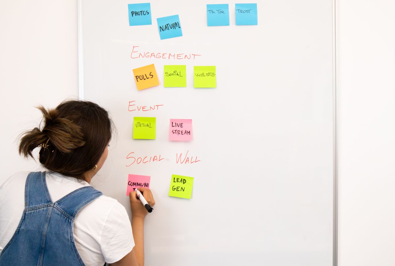 A woman arranging notes on a whiteboard with colorful sticky notes in an office setting.